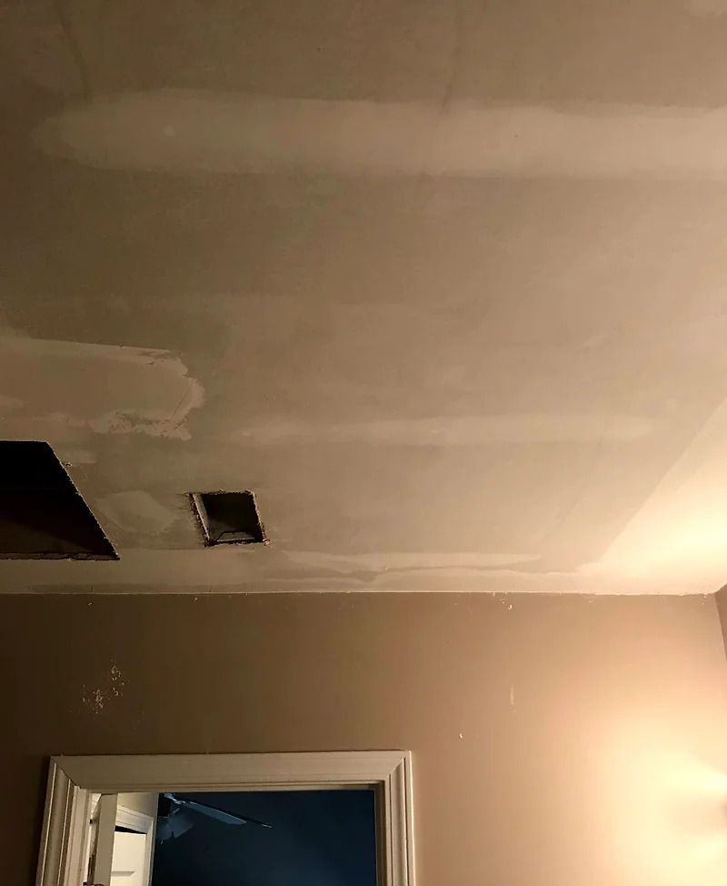 Ceiling with patched drywall and air vent; tan wall, doorway below.