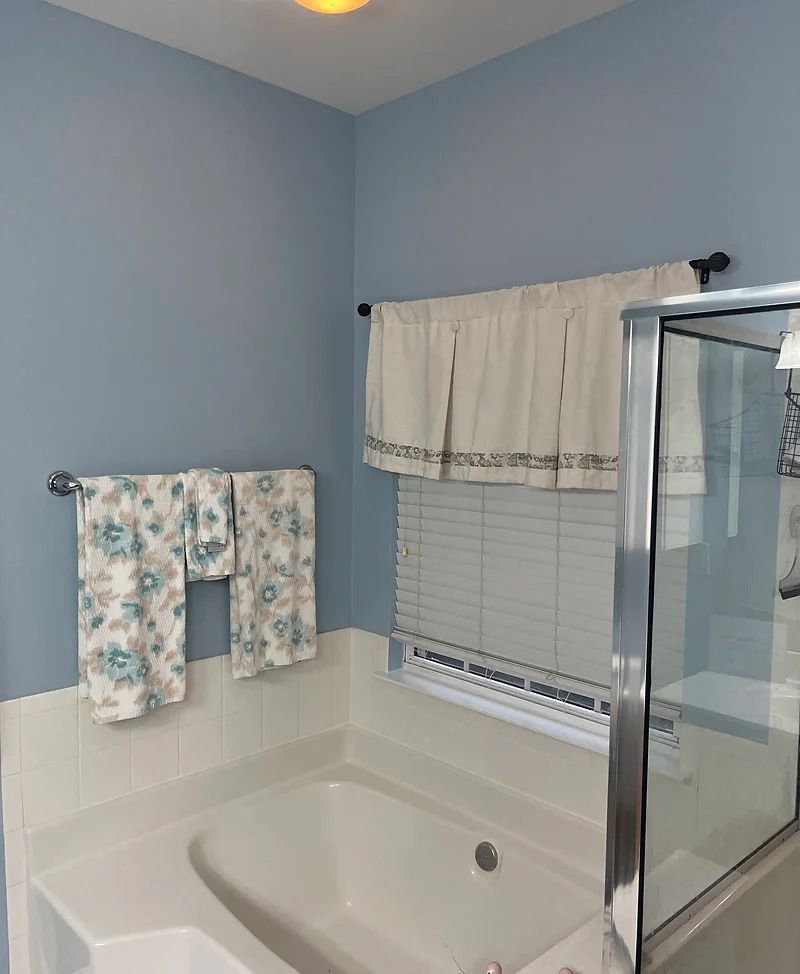 Bathroom with blue walls, white bathtub, floral towels, and a shower door.
