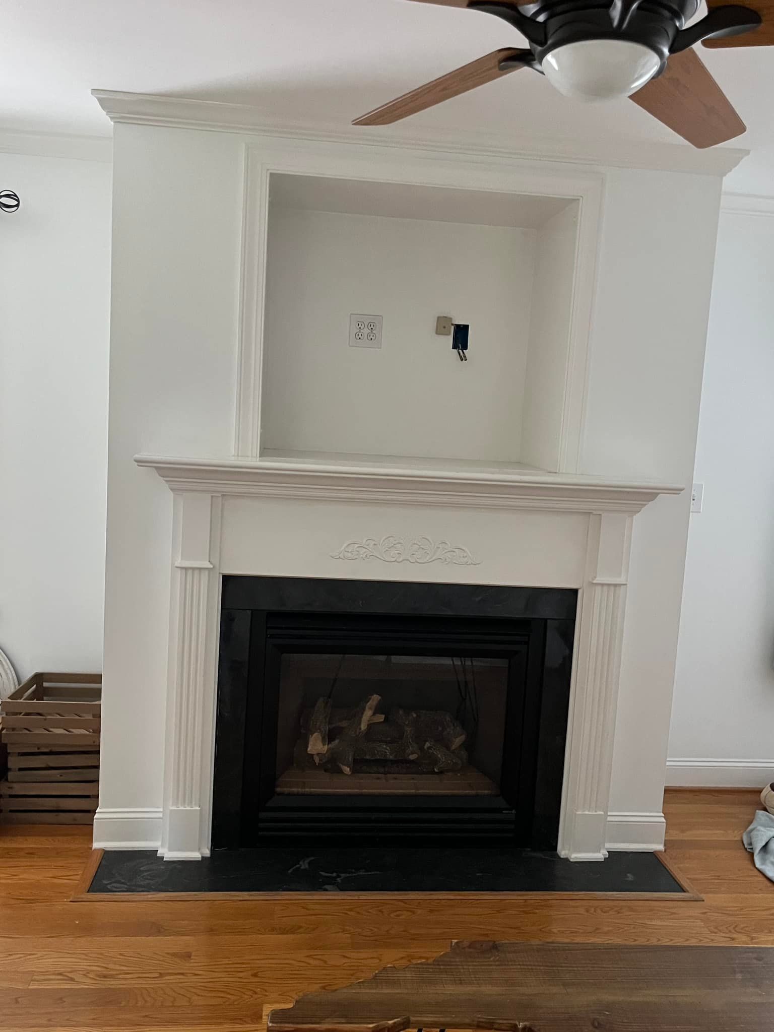 White fireplace with a black firebox and an open niche above. Wooden floor.