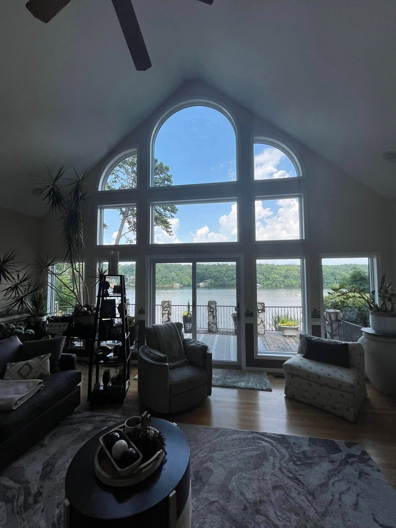 Spacious living room with large windows overlooking a lake, featuring furniture and natural light.