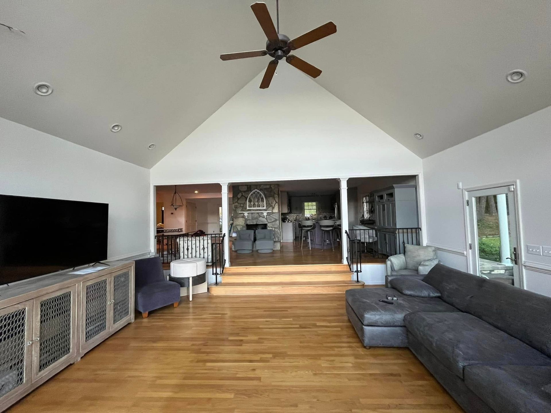 Spacious living room with vaulted ceiling, hardwood floors, and a large TV; opens to other rooms.