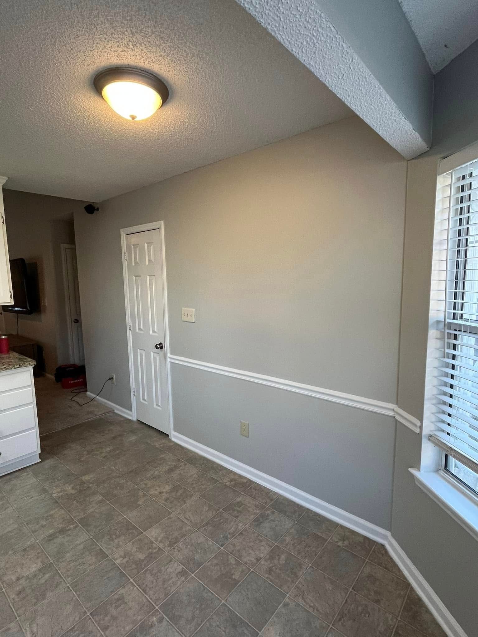 Light gray dining room with a door, window, and trim. A beige tiled floor and a recessed light fixture are visible.