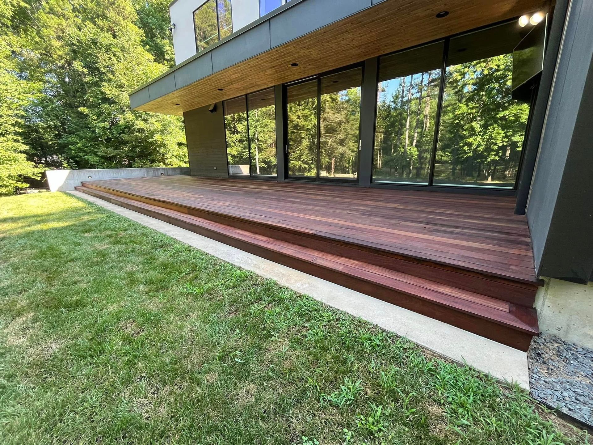 Paint can with brush on a stained wooden deck; half-stained with rich brown color.