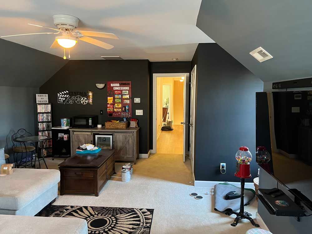 A dark-walled room with a seating area, entertainment center, and a doorway to a brighter space.