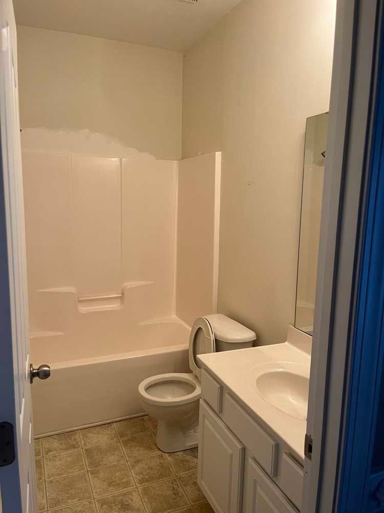 Bathroom with a pink tub/shower, white toilet, vanity, and beige flooring.