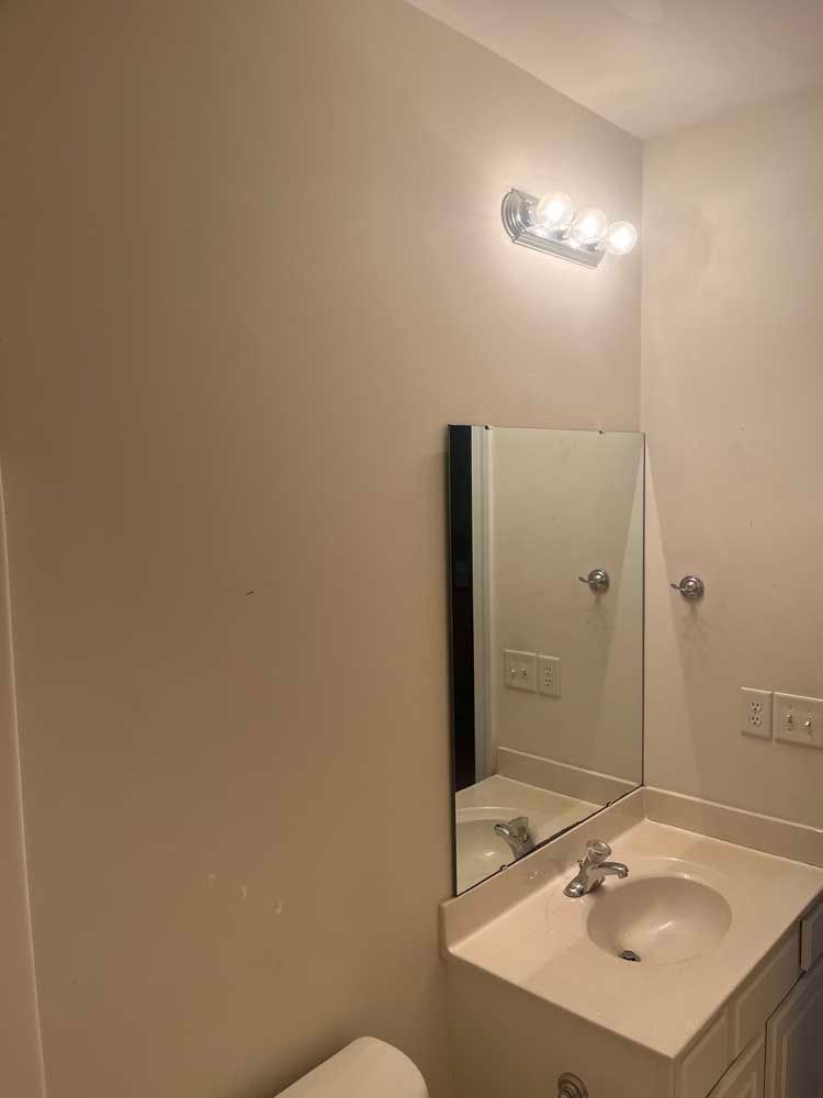 Bathroom with sink, mirror, and light fixture. Cream-colored walls, white vanity, and silver fixtures.
