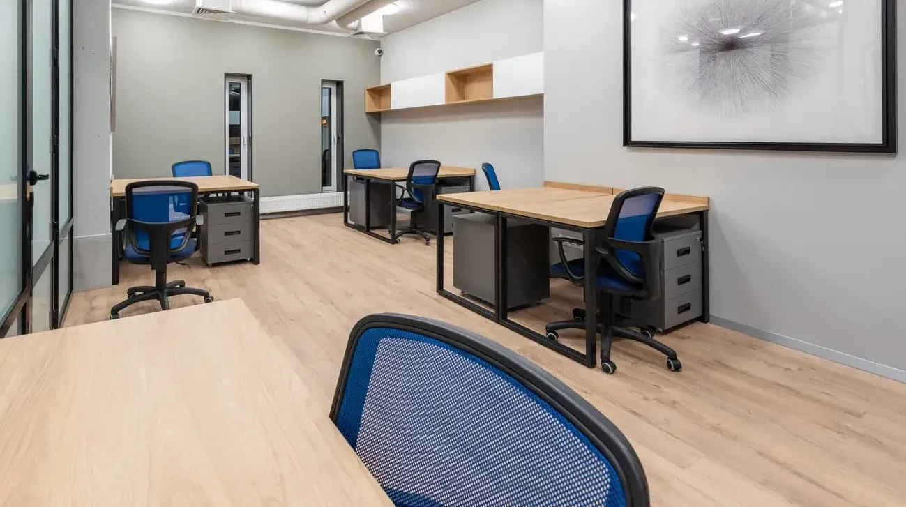 Office with light wood desks, blue chairs, gray filing cabinets, and neutral walls.