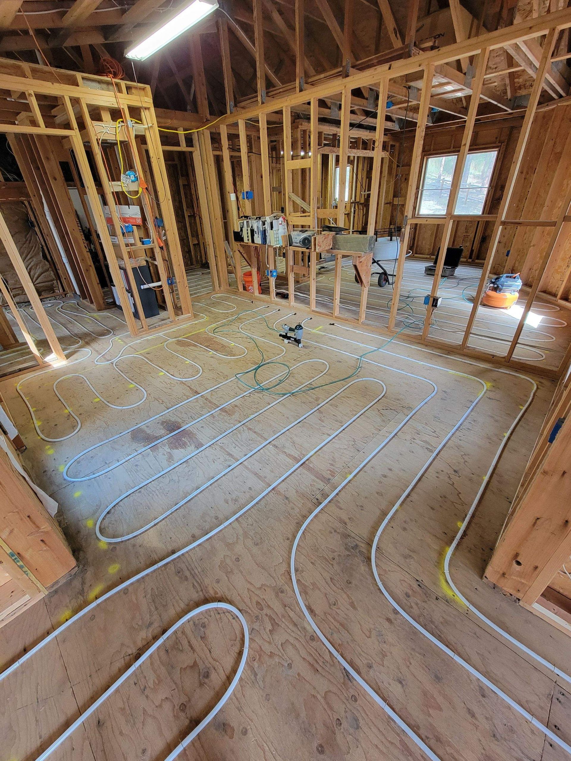 Framing of room with white tubing for radiant floor heating on wooden subfloor.