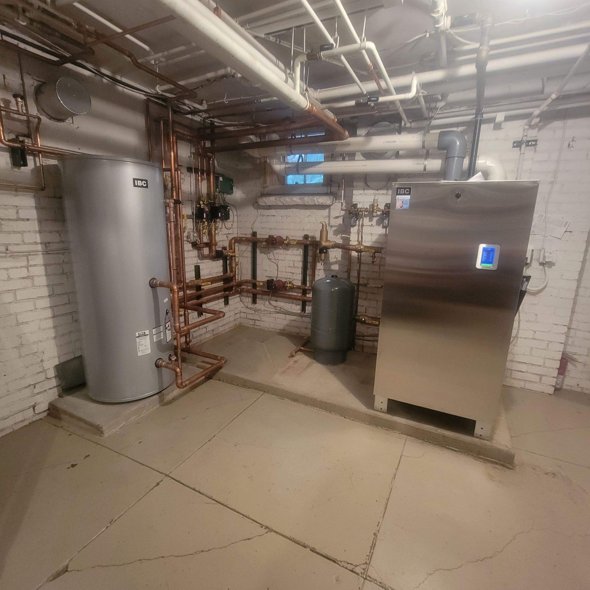 Two cylindrical water heaters on a metal platform, with copper pipes and energy efficiency stickers in a utility room.