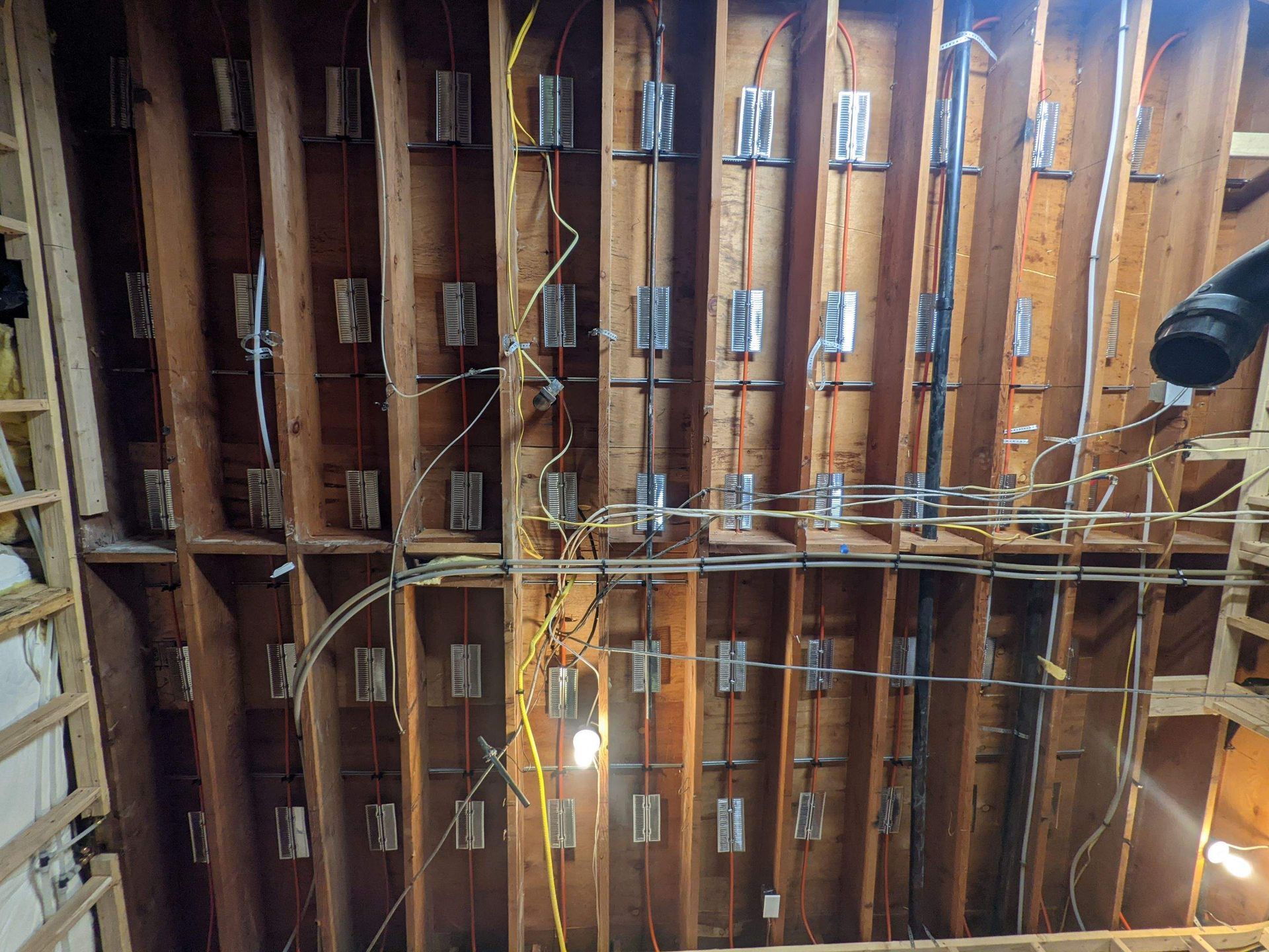 Orange radiant floor tubing with metal convective fins in joist bays