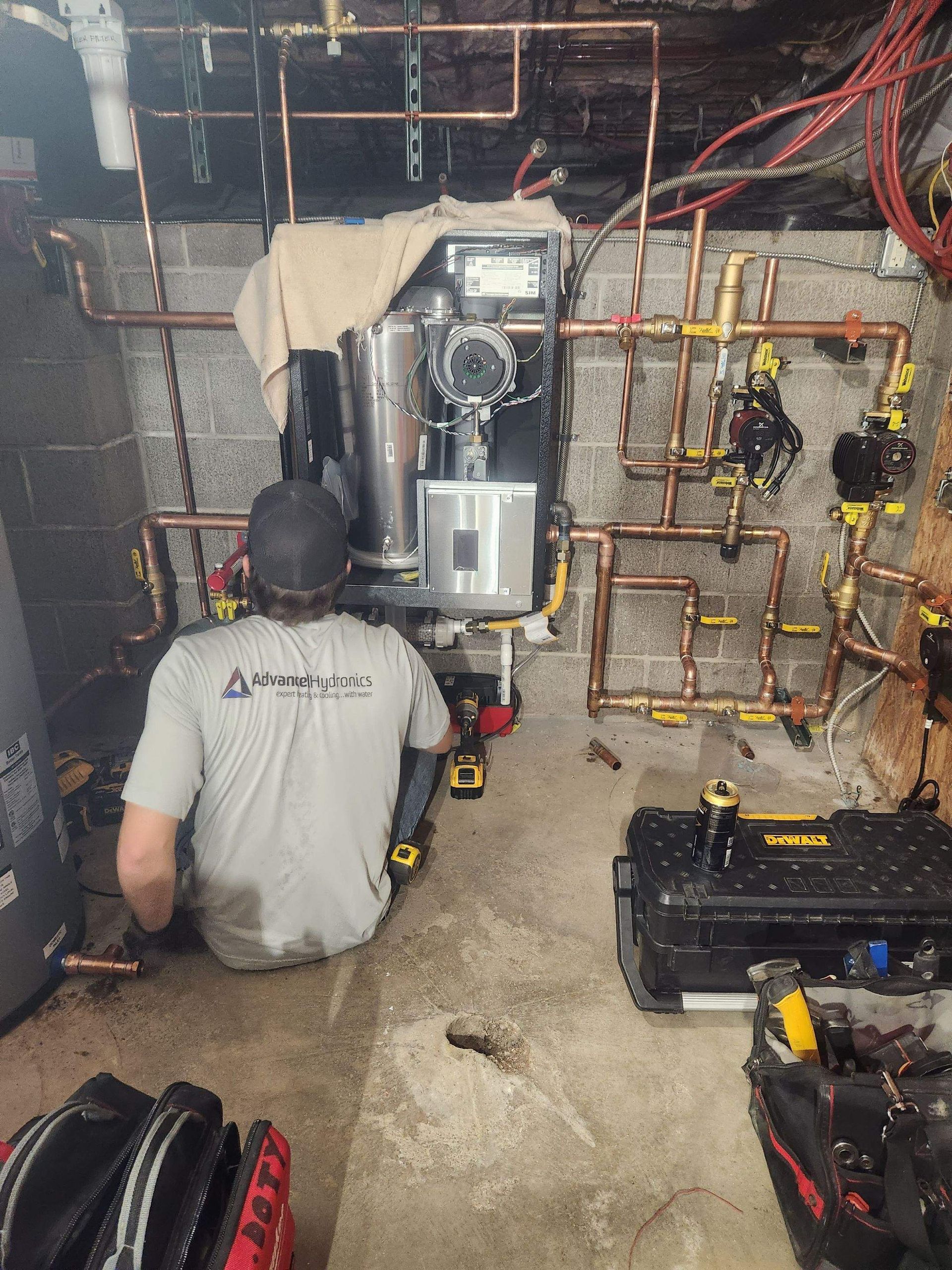 A plumber works on copper pipes and a boiler in a basement.
