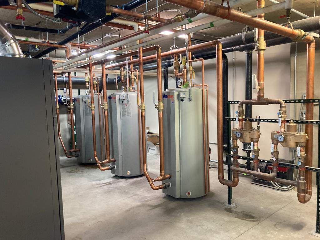 Interior view of mechanical room with pipes, tanks, and electrical components on exposed wooden walls.