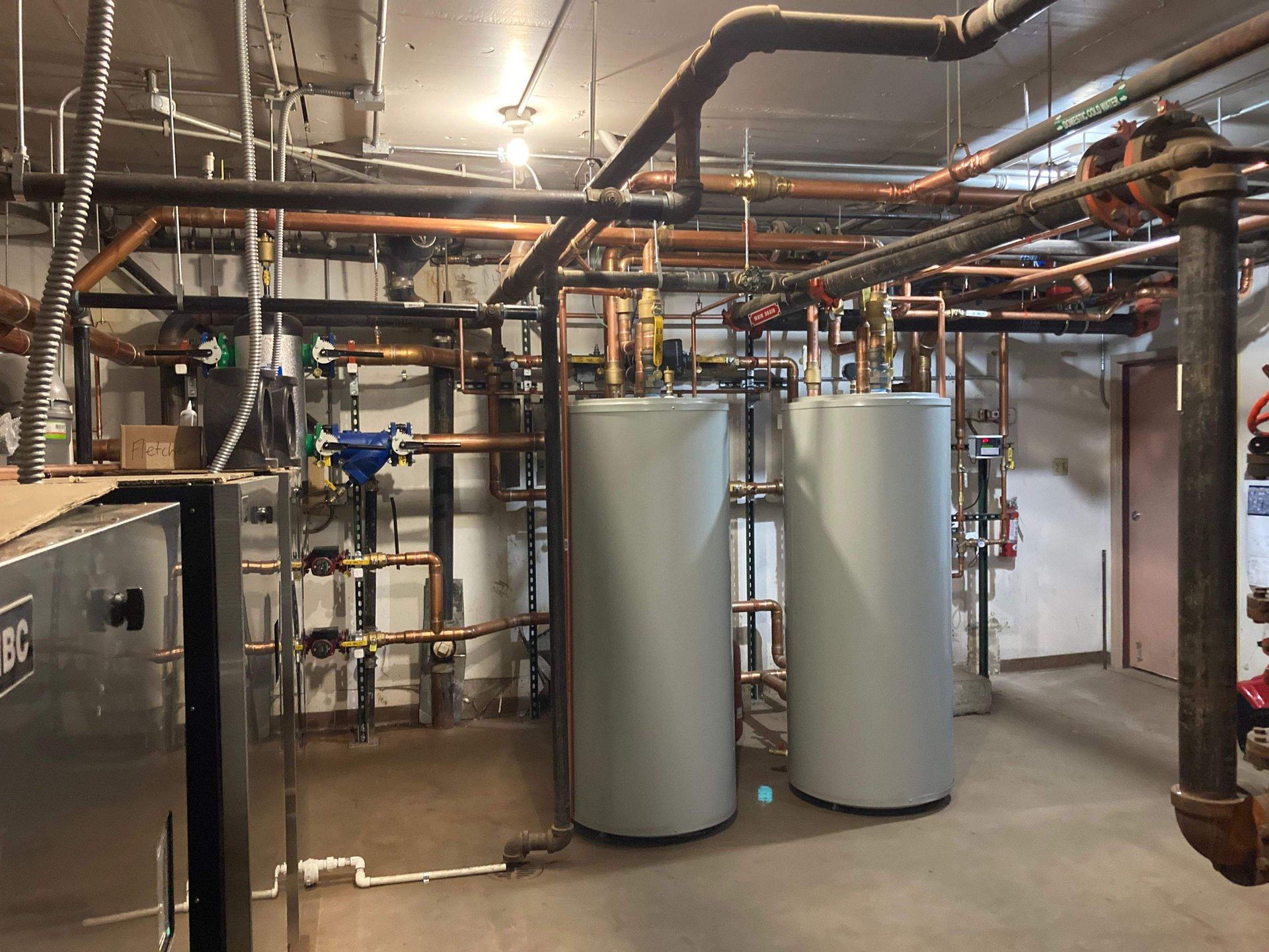 Copper pipes and a white tank on a concrete wall with insulation and wooden beams.