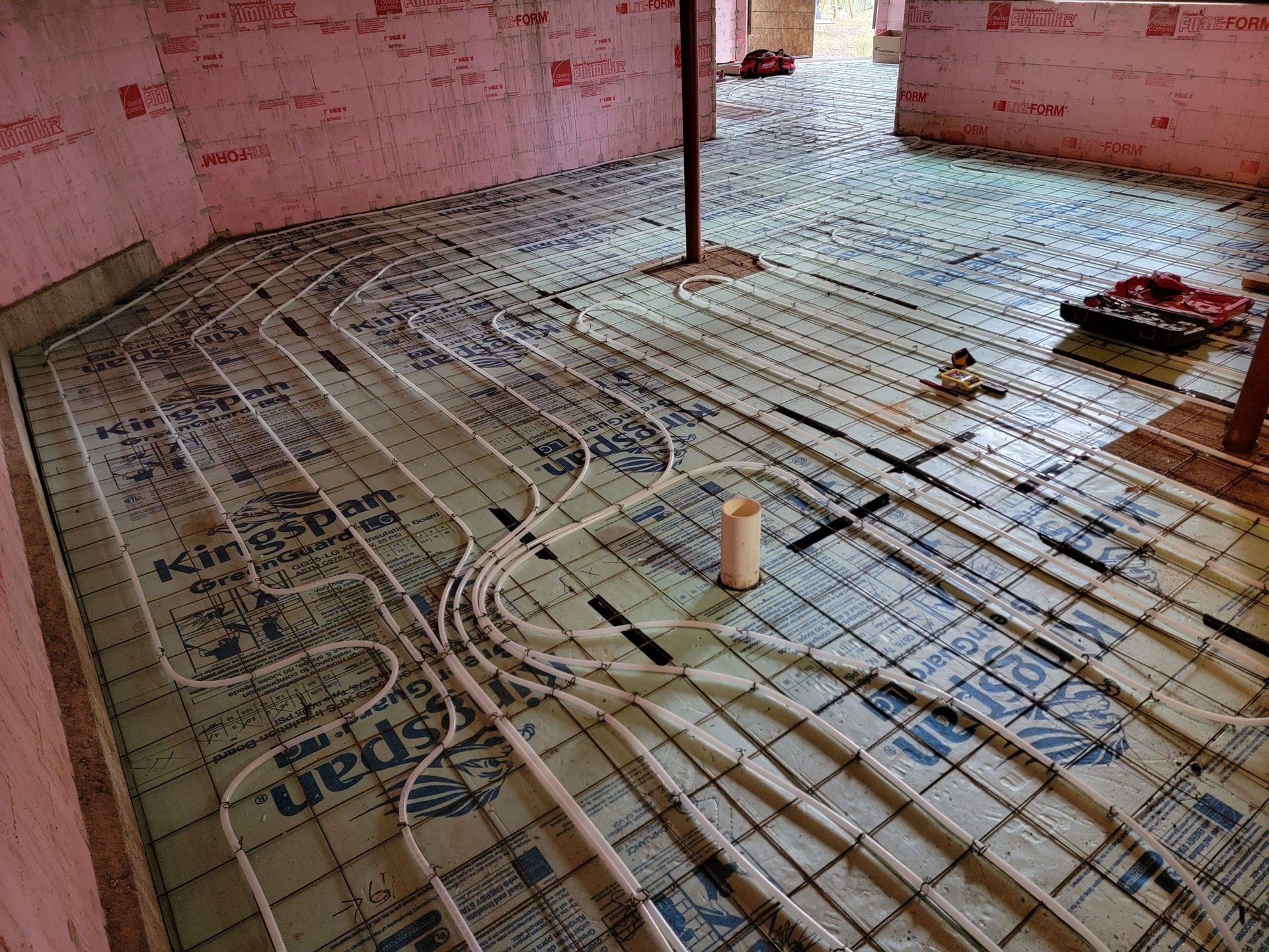 Pipes laid in a grid on insulation, prepped for radiant floor heating installation in a room.