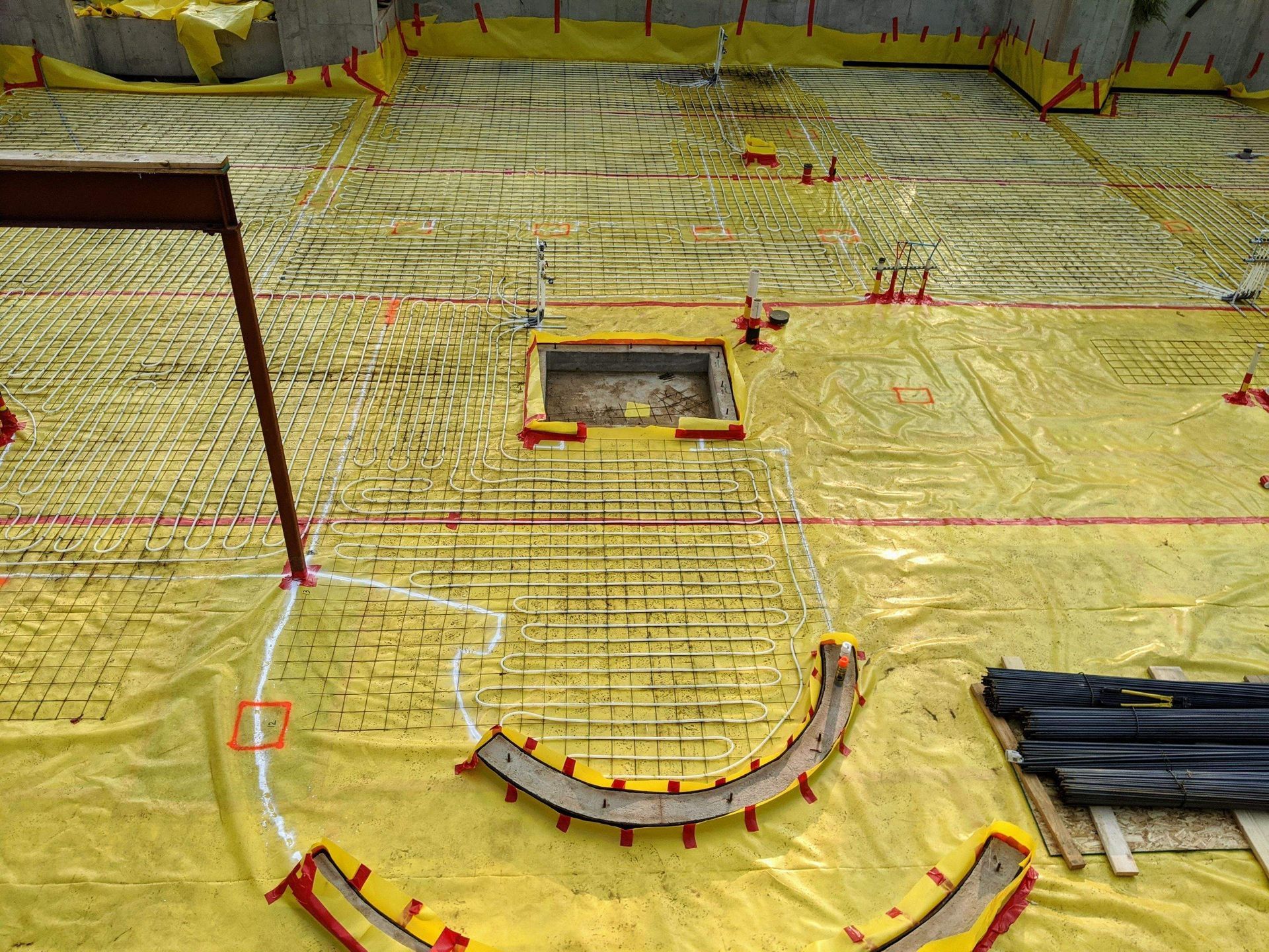 Construction site with yellow tarp, rebar grid, and curved wood forms.