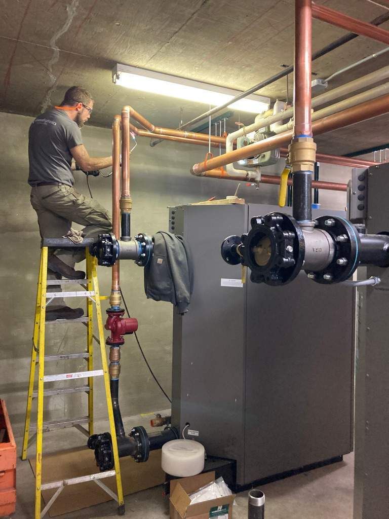Plumbing room: Two water heaters, a heater, and copper pipes against a concrete wall.