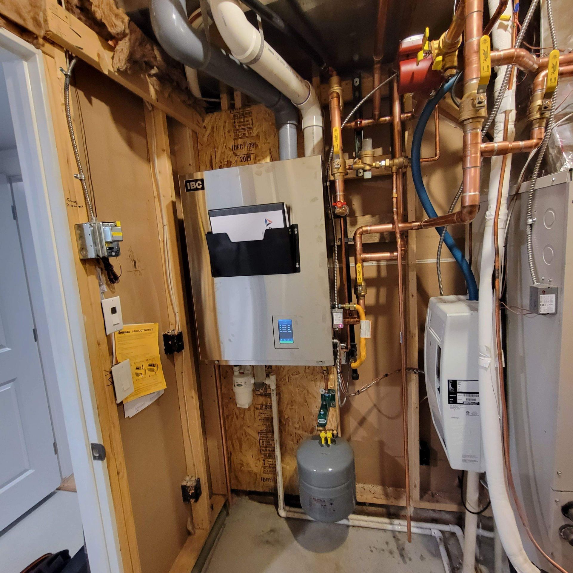 A utility room with a water heater, pipes, and a pressure tank; neutral colors dominate.