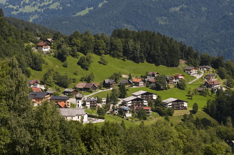 Ein kleines Dorf liegt auf einem Hügel, umgeben von Bäumen.