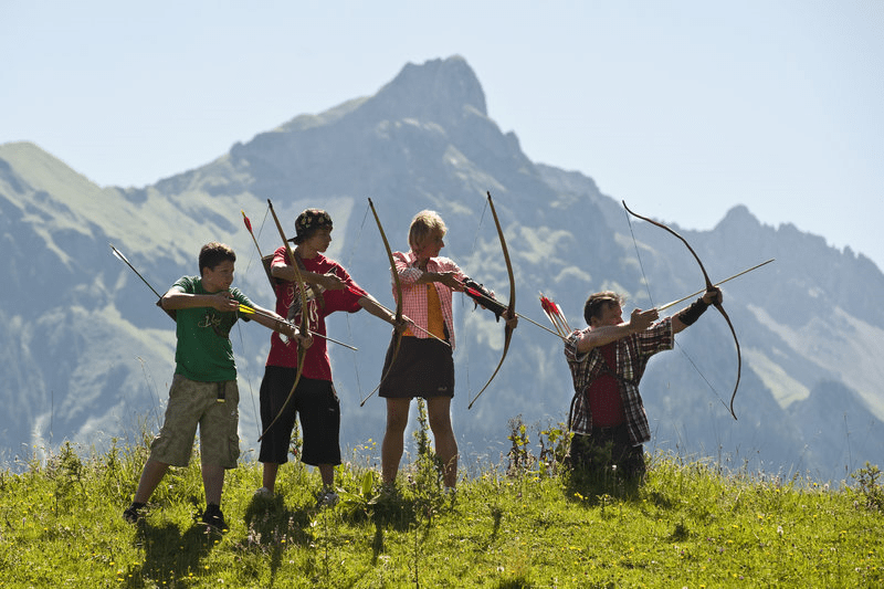 Eine Gruppe Leute übt Bogenschießen in den Bergen.