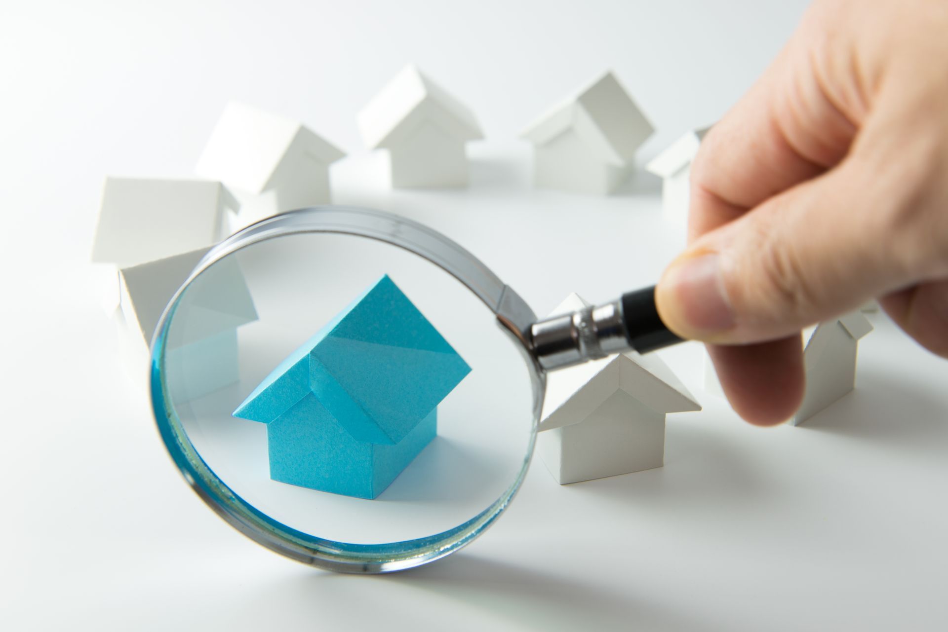 A person is holding a magnifying glass over a model house.