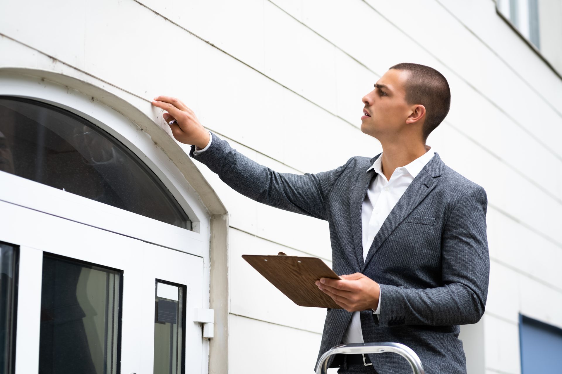 A man in a suit is standing in front of a building holding a clipboard.
