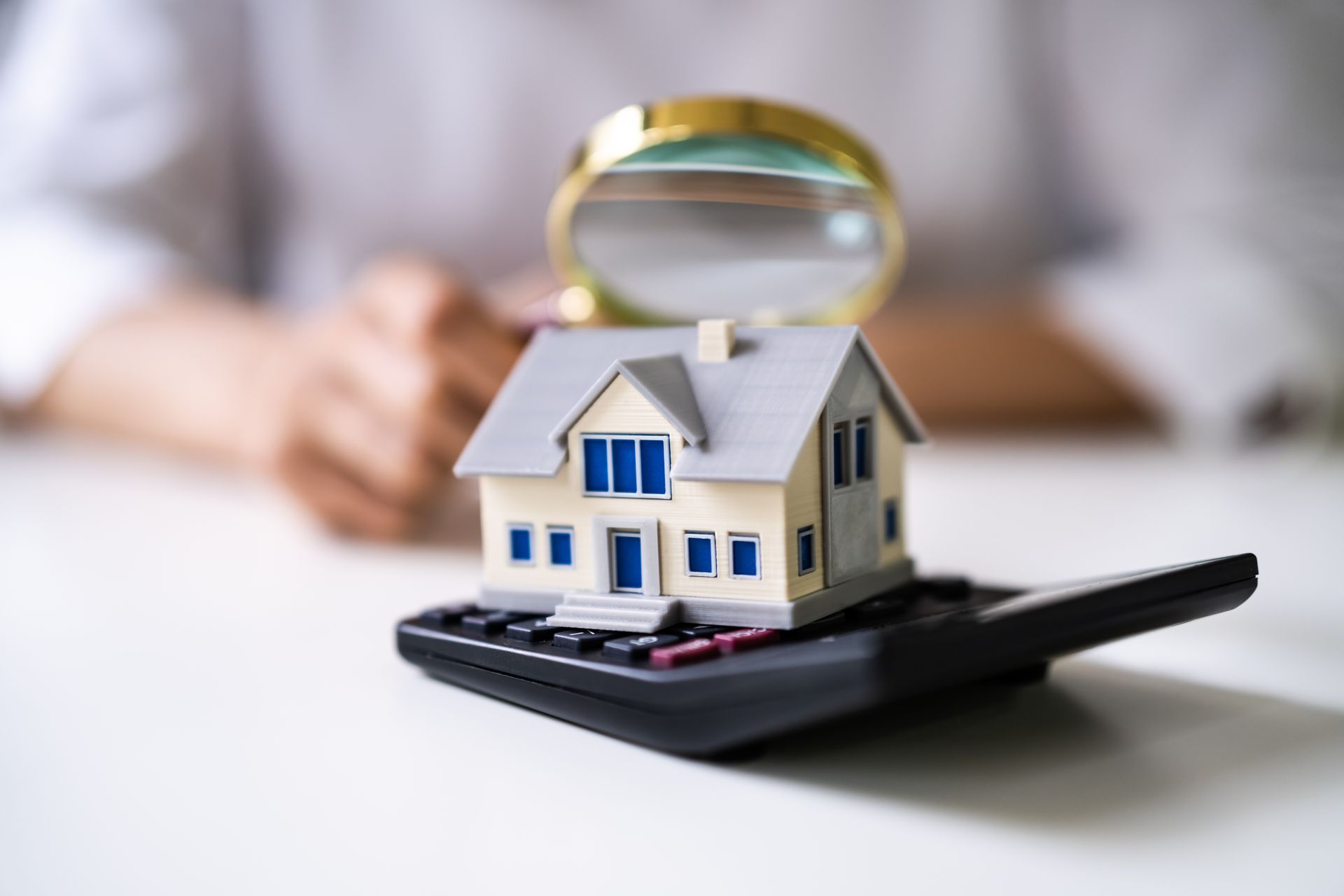 A model house is sitting on top of a calculator with a magnifying glass.