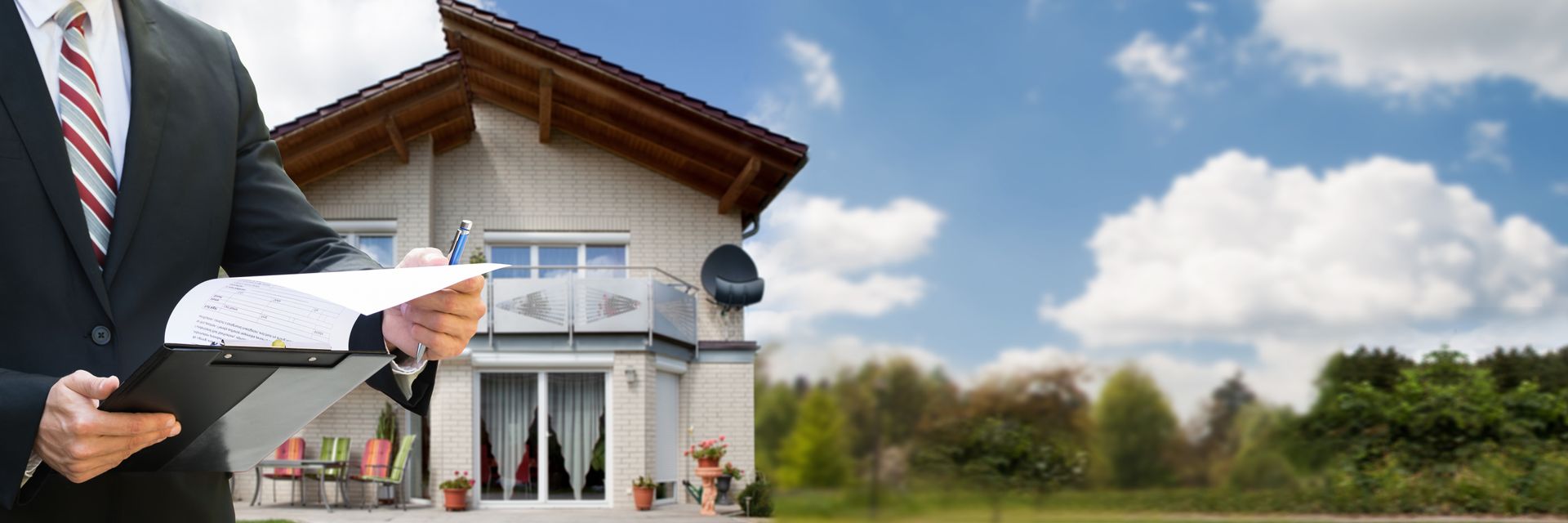 A man in a suit and tie is holding a piece of paper in front of a house.