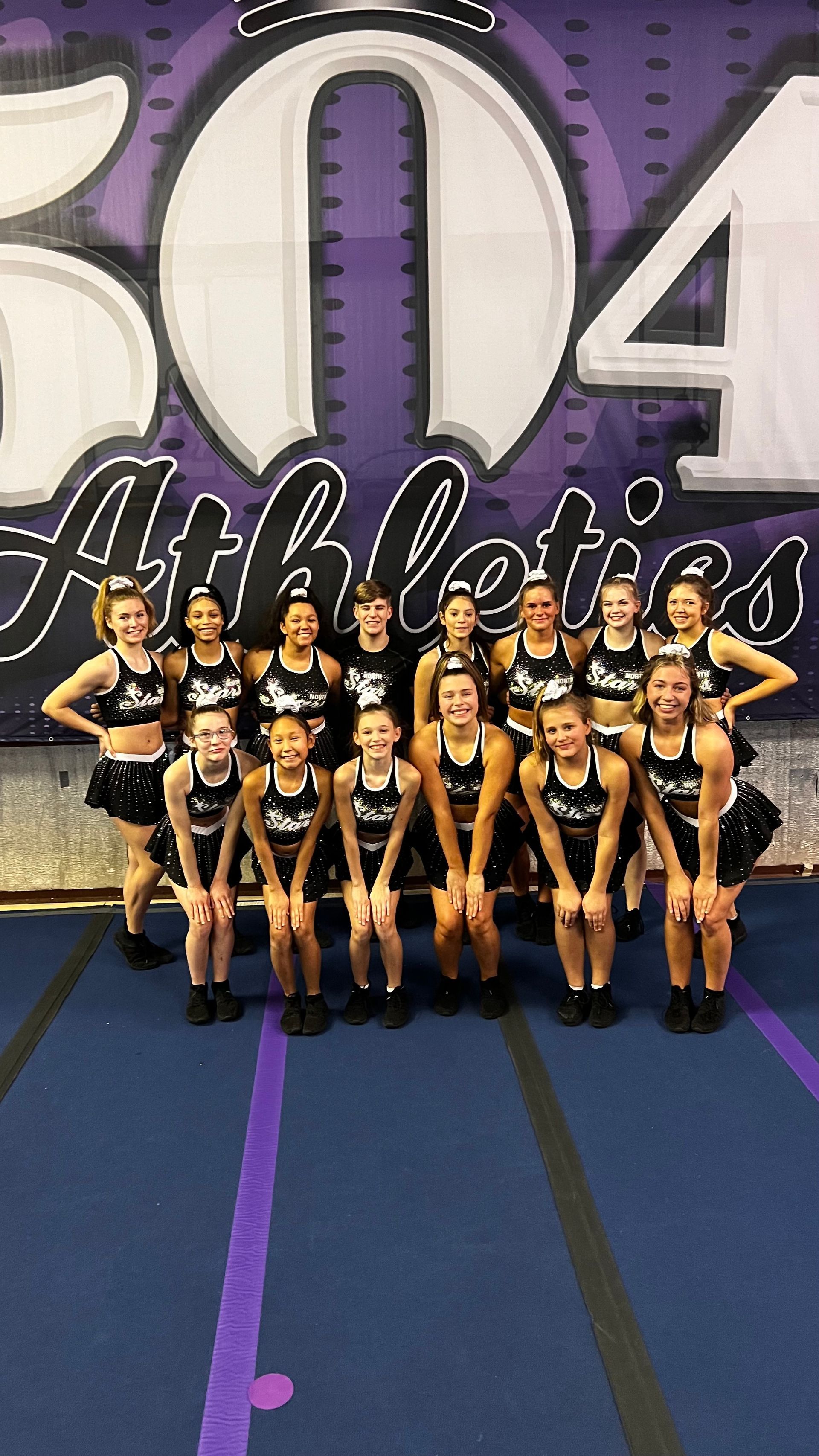 A group of cheerleaders are posing for a picture in front of a purple banner.