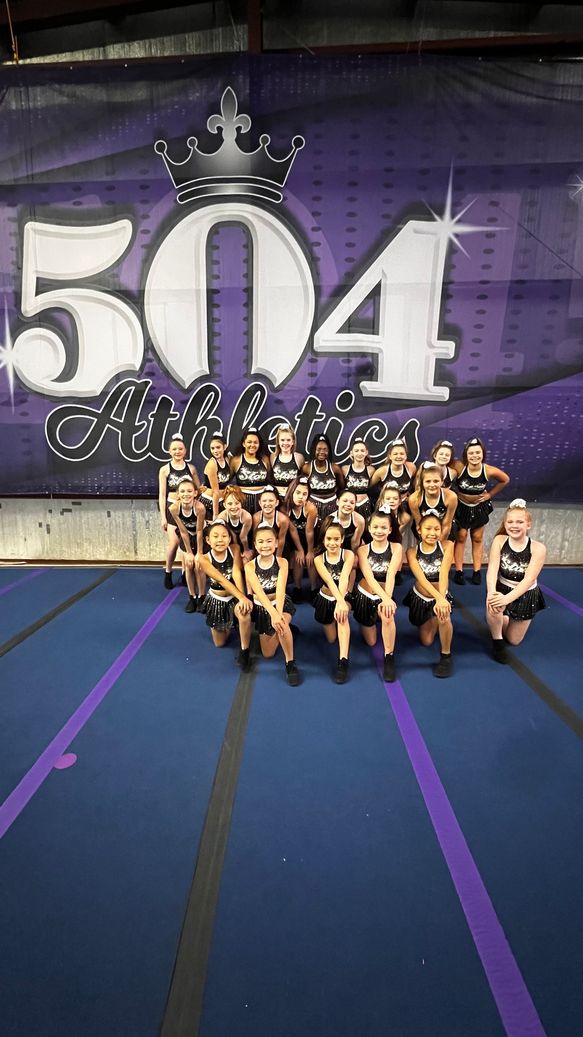 A group of cheerleaders are posing for a picture in front of a purple banner.