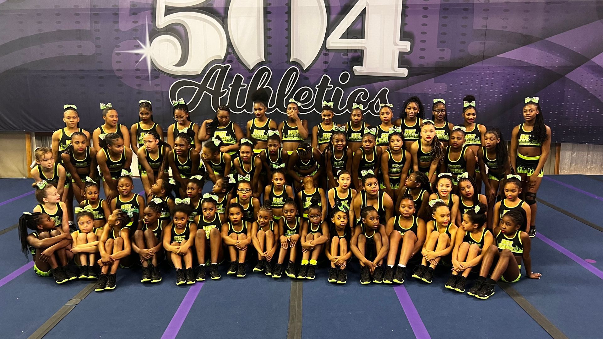 A group of cheerleaders are posing for a picture in front of a sign that says 514 athletics.