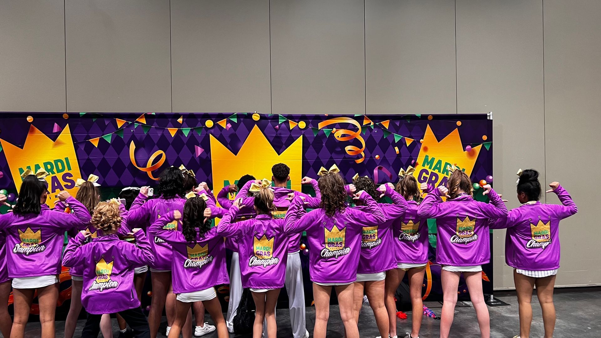 A group of cheerleaders are standing in front of a mardi gras banner.