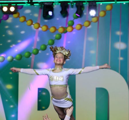 A little girl in a cheerleading outfit is performing on stage