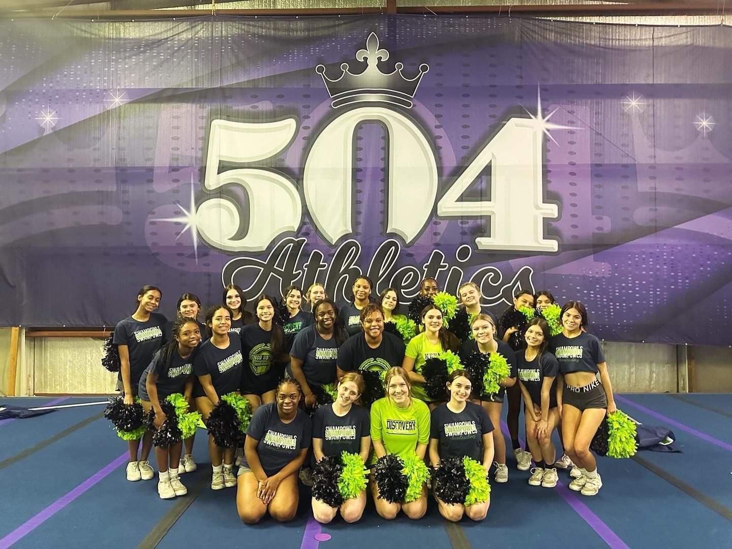 A group of cheerleaders are posing for a picture in front of a 504 athletics banner.