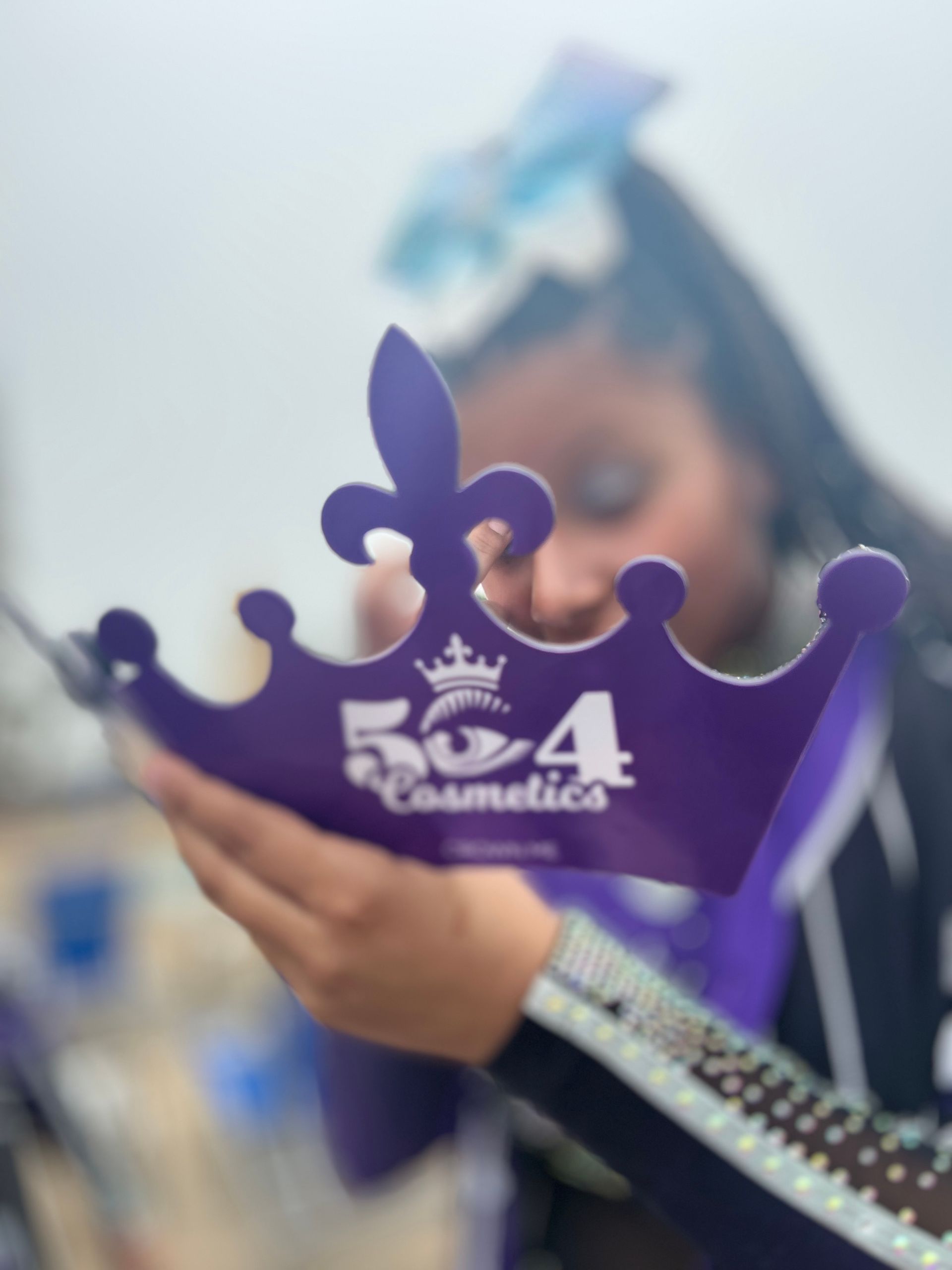 A woman is holding a purple crown that says 504 cosmetics