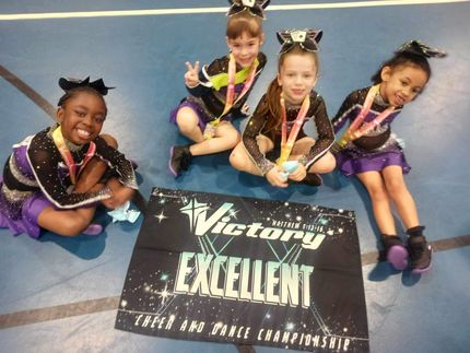 Four cheerleaders sitting next to a victory excellent banner