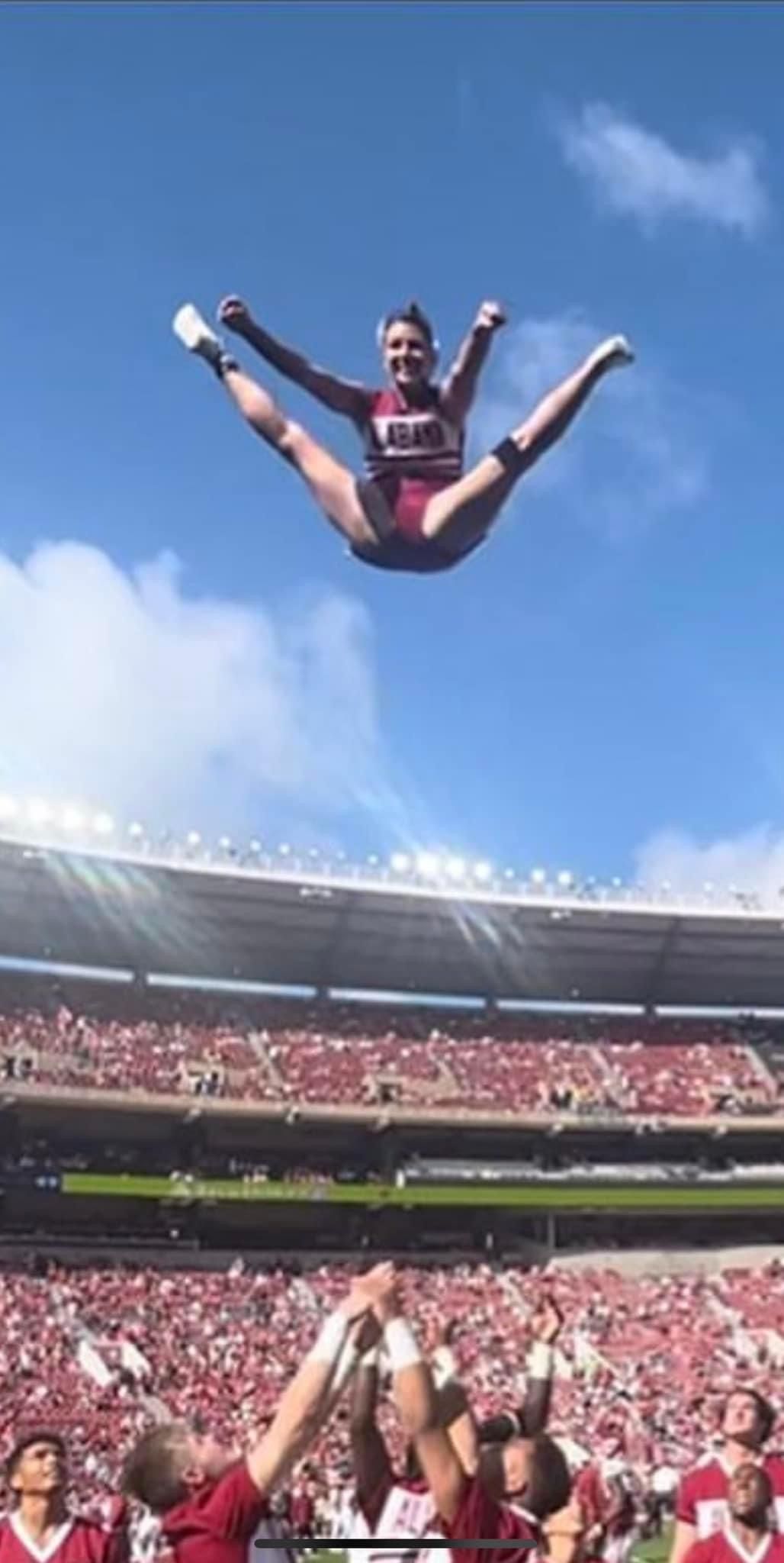 A cheerleader is jumping in the air at a football game