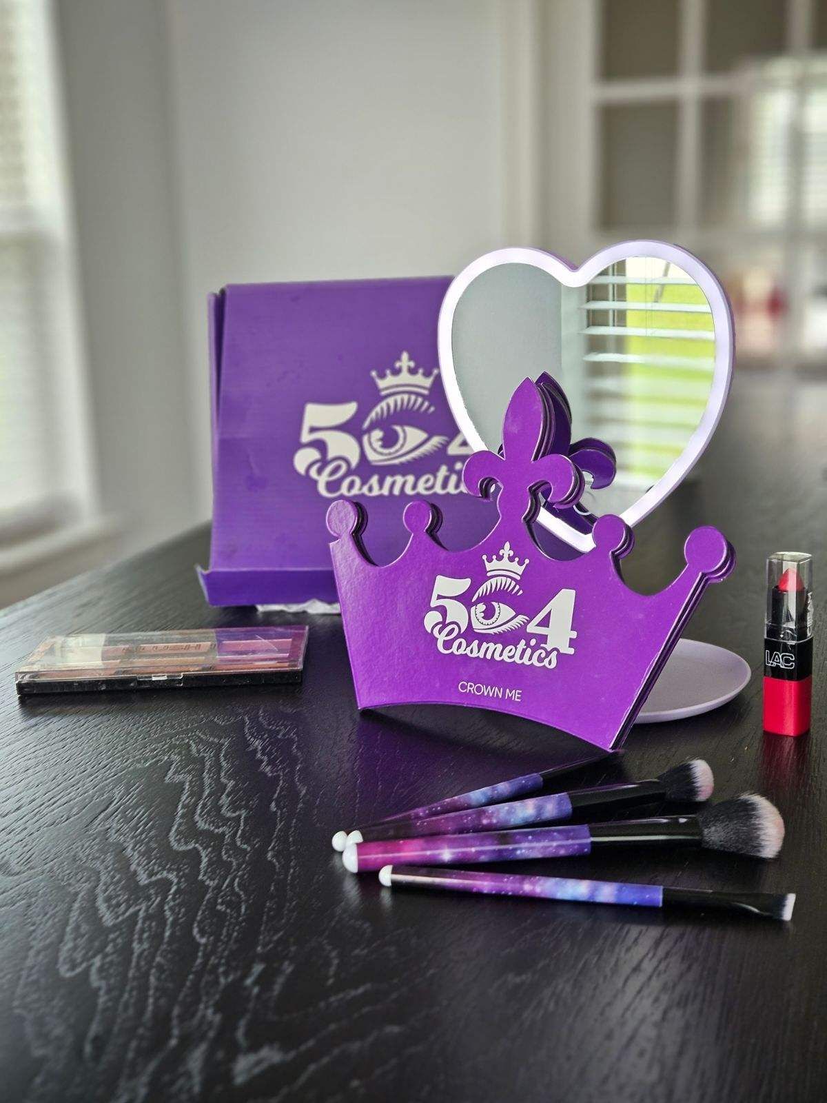 A purple crown shaped mirror and brushes are on a table.