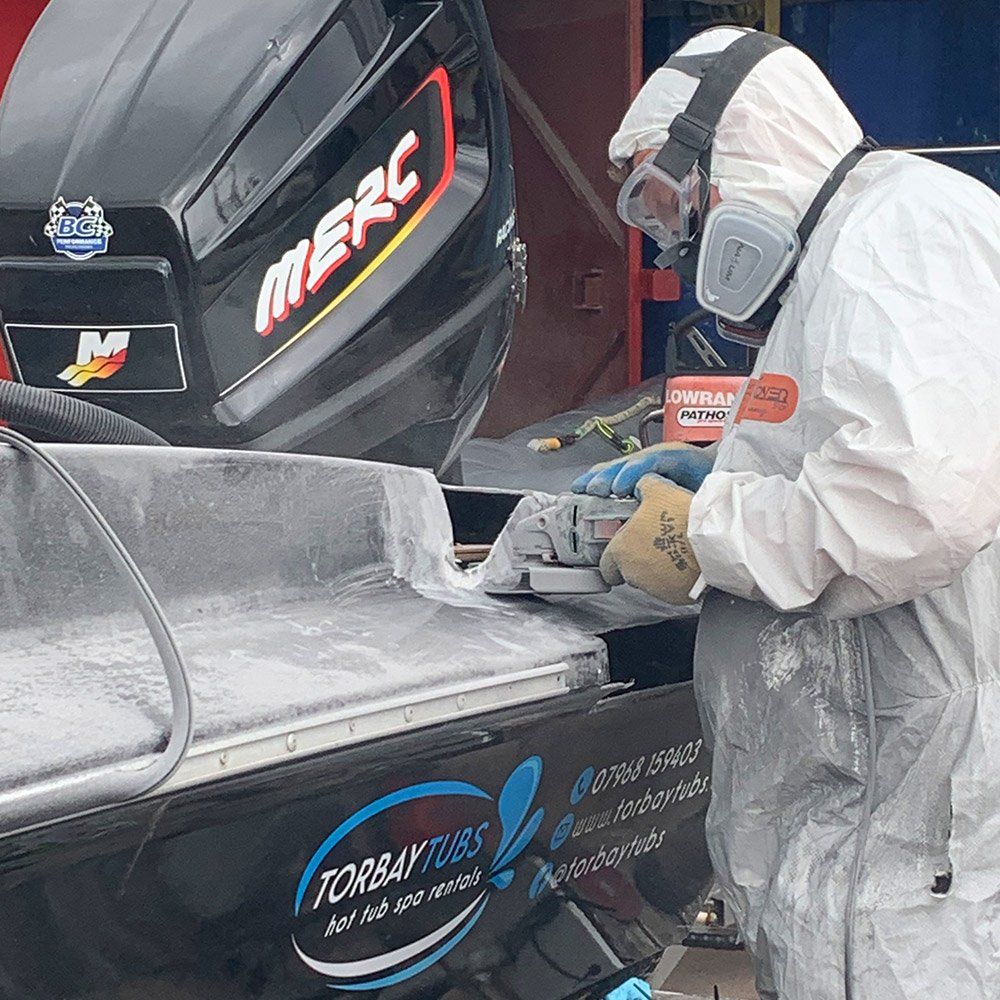 a man in a protective suit is working on a boat with a merc engine in the background