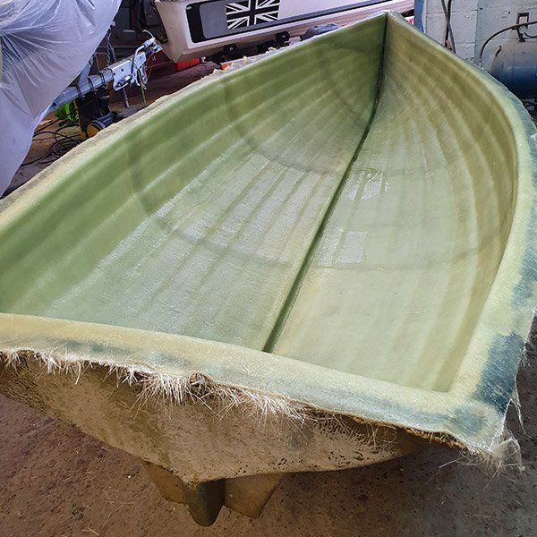 a green boat is sitting on the ground in a garage .