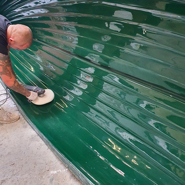 a man is polishing a green boat with a polisher .
