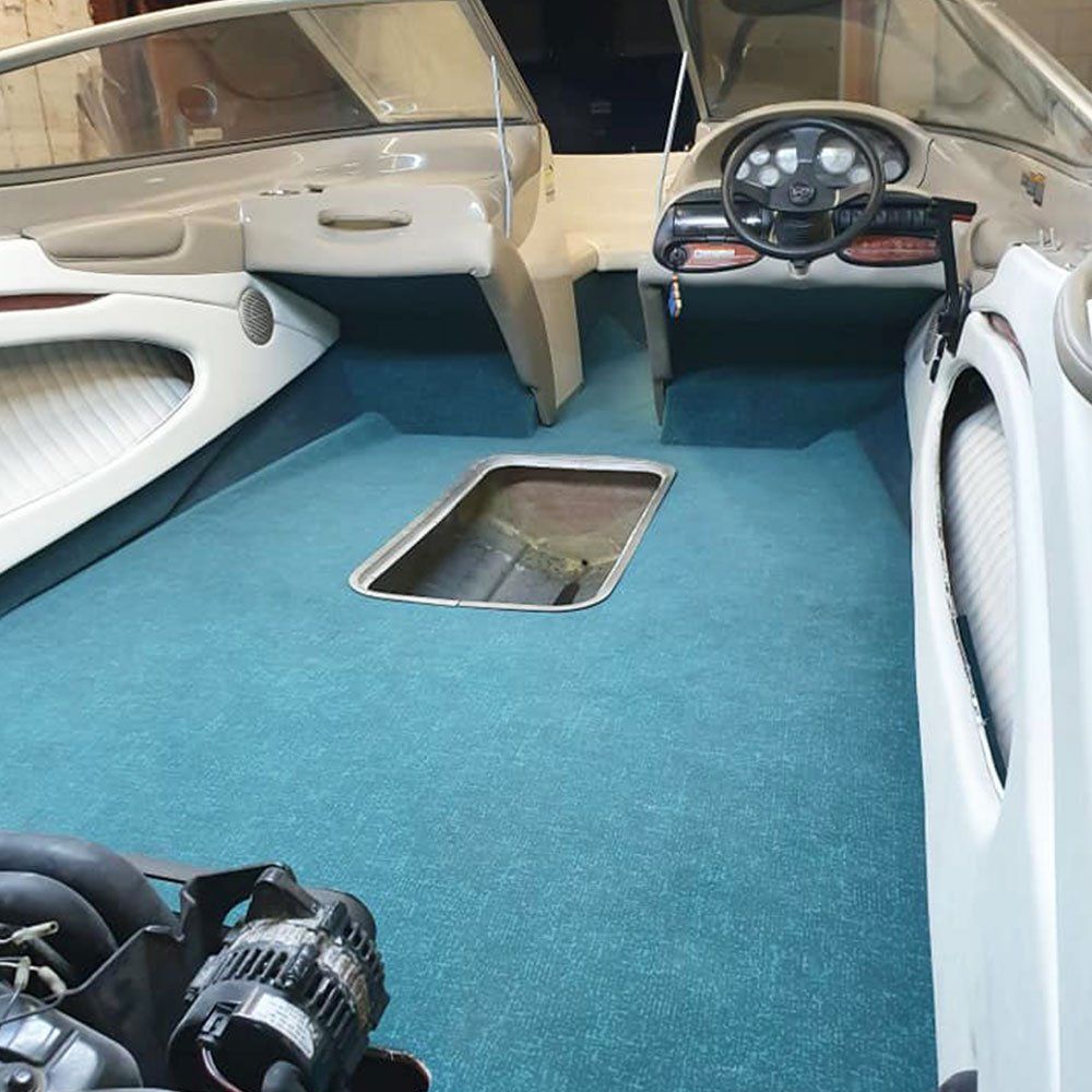 the inside of a boat with a blue carpet and a steering wheel