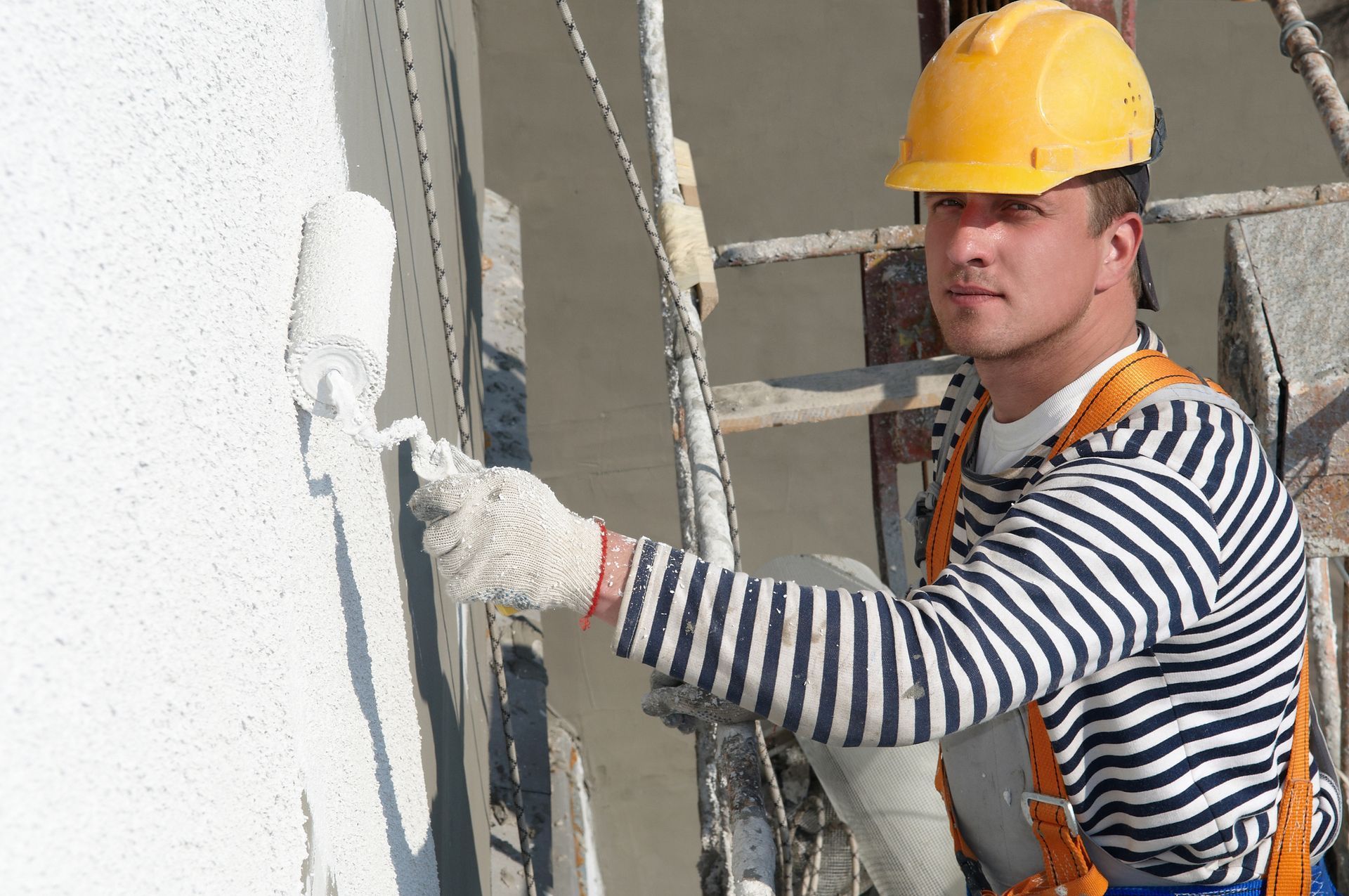 Construction worker using paint roller to apply white paint on exterior wall