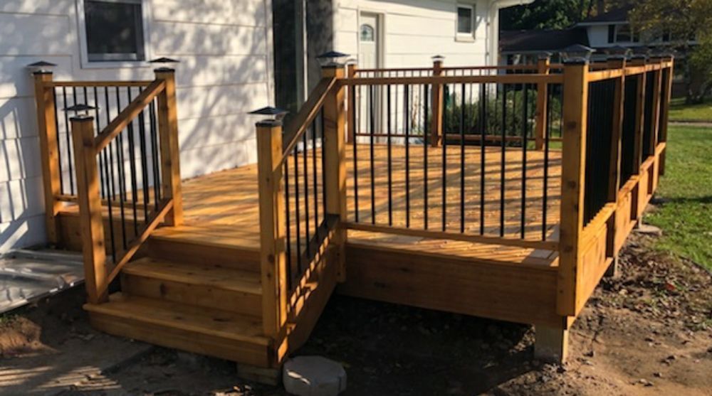 A wooden deck with stairs and a metal railing is in front of a white house.