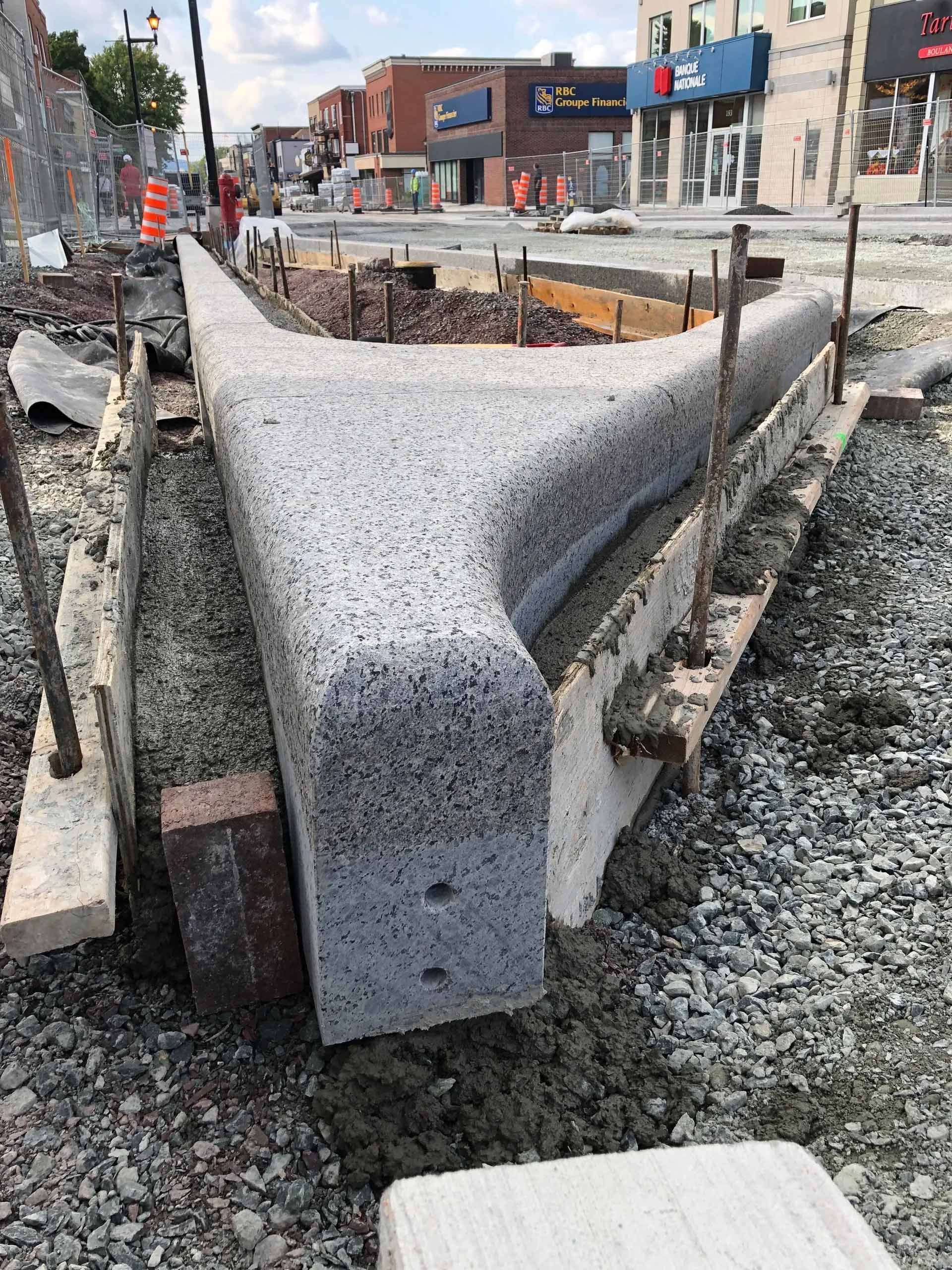 Construction d'une bordure en béton en milieu urbain. La bordure grise est réalisée à l'aide de supports en bois et d'armatures.