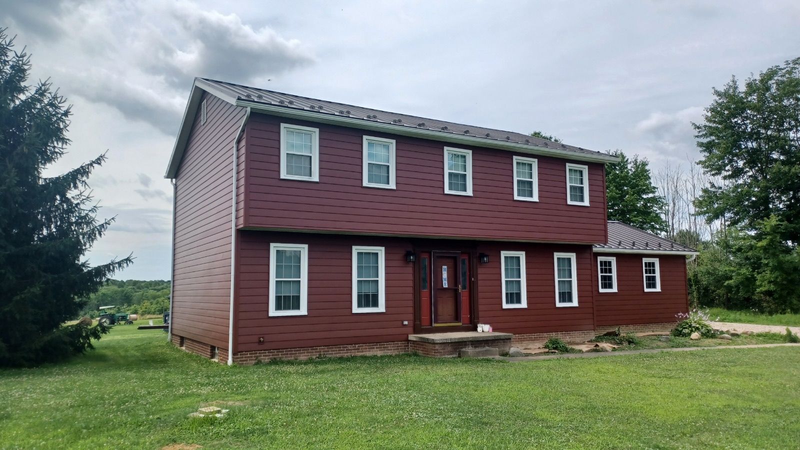 A red house with white windows is sitting on top of a lush green field.