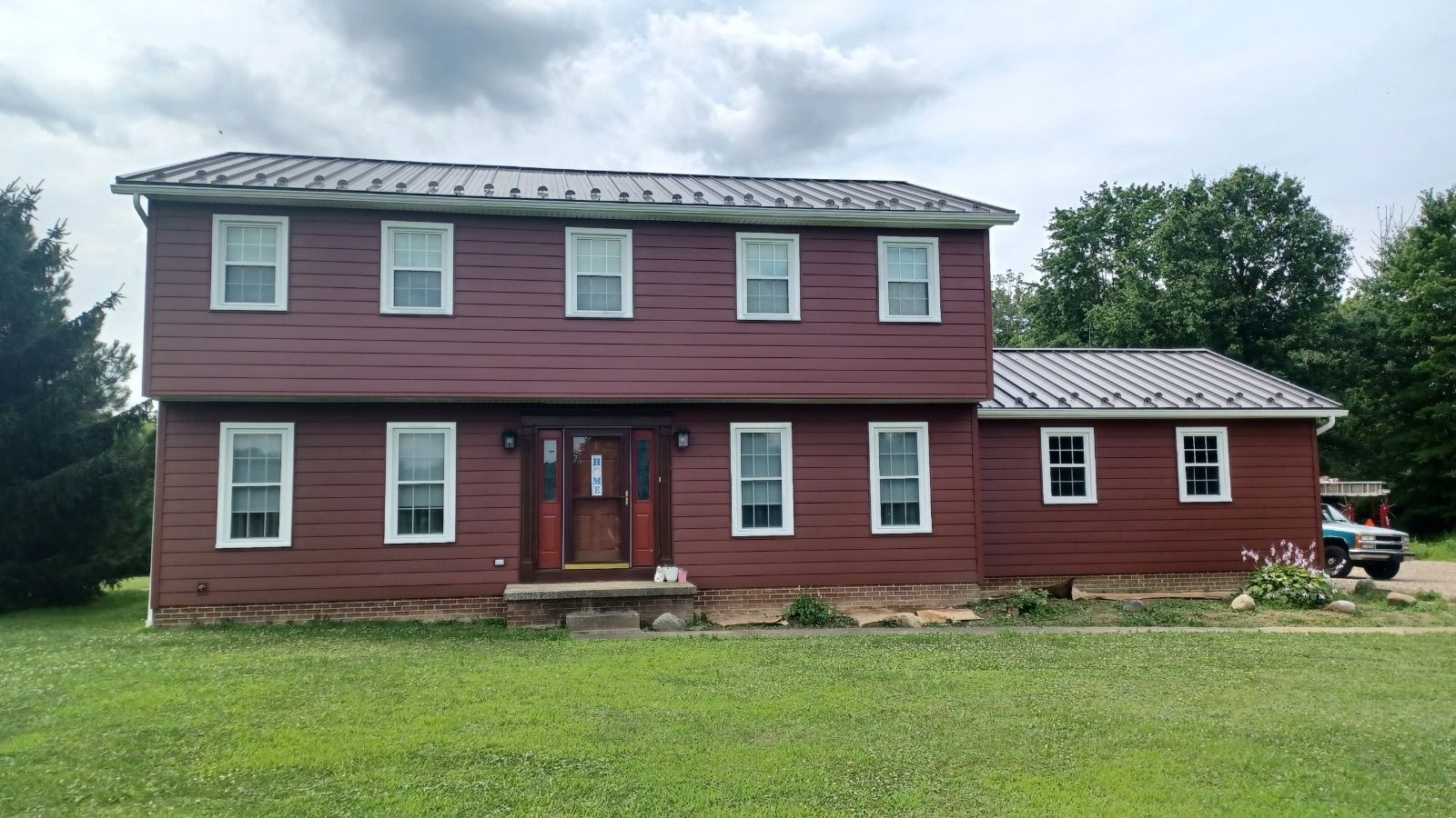 A large red house with a gray roof is sitting on top of a lush green field.