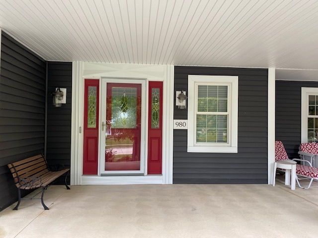 The front porch of a house with a red door and a bench