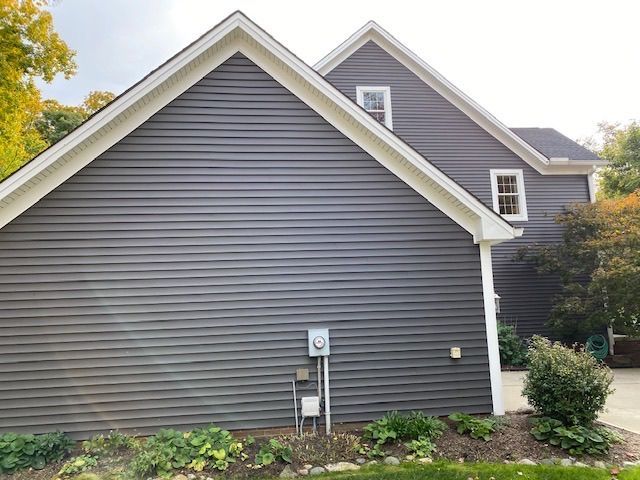 The side of a house with a gray siding and a white trim.