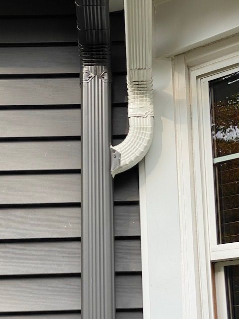 A white gutter on the side of a house next to a window.