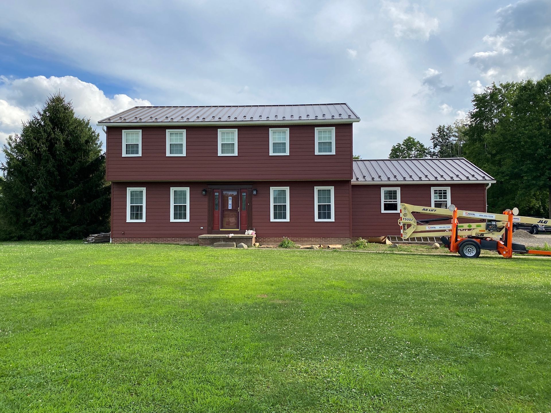 A large red house with a metal roof is sitting on top of a lush green field.